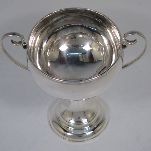 A small but handsome Sterling Silver trophy cup, having a plain round bellied body, with two scroll side-handles, and all sitting on a pedestal foot. Made by the Adie Brothers of Birmingham in 1928. The dimensions of this fine hand-made silver trophy cup are height 15 cms (6 inches), spread across arms 15 cms (6 inches), and it weighs approx. 148g (4.8 troy ounces).   