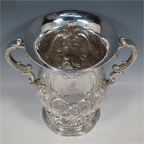 An impressive Antique Victorian Sterling Silver trophy cup, in a Campana style, having a bellied body with cartouches on both sides, with hand-chased floral and scroll decoration, with two floral scroll handles, and sitting on a pedestal foot. This beautiful antique silver trophy cup was made by Charles Boyton of London in 1861. The dimensions of this fine hand-made antique silver trophy cup are height 26 cms (10.25 inches), spread across handles 30 cms (11.75 inches), and it weighs approx. 1,291g (42 troy ounces). Please note that this item is crested on one side. 