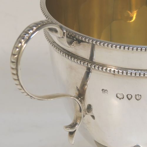 A small but very elegant Antique Victorian Sterling Silver trophy cup in a George III neoclassical style, having a round plain body with tapering sides, a gold-gilt interior, with two applied bead top borders, two scroll side-handles,  and all sitting on a pedestal foot with a square base. This handsome antique silver trophy cup was made by Angel and Savory of London in 1890. The dimensions of this fine hand-made antique silver trophy cup are height 12 cms (4.75 inches), spread across arms 16 cms (6.3 inches), and it weighs approx. 182g (5.9 troy ounces).  