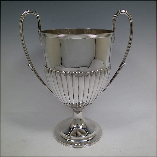 A very handsome Antique Victorian Sterling Silver trophy cup in a George III neoclassical style, having a round body with tapering sides and half-fluted decoration, with hand-chased reeded borders, two looped side-handles with anthemion leaves, and all sitting on a pedestal foot. Made by Charles Stuart Harris of London in 1895. The dimensions of this fine hand-made antique silver trophy cup are height 32.5 cms (12.75 inches), spread across arms 26.5 cms (10.5 inches), and it weighs approx. 940g (30 troy ounces).    