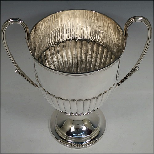 A very handsome Antique Victorian Sterling Silver trophy cup in a George III neoclassical style, having a round body with tapering sides and half-fluted decoration, with hand-chased reeded borders, two looped side-handles with anthemion leaves, and all sitting on a pedestal foot. Made by Charles Stuart Harris of London in 1895. The dimensions of this fine hand-made antique silver trophy cup are height 32.5 cms (12.75 inches), spread across arms 26.5 cms (10.5 inches), and it weighs approx. 940g (30 troy ounces).    