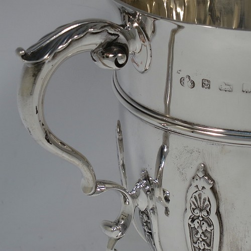 A very handsome Antique Edwardian Sterling Silver trophy cup, in a George II style, having a round body with applied floral strap-work decoration, two scroll side-handles with anthemion leaf thumb-pieces, a central applied girdle band, and all sitting on a stepped pedestal foot. Made by Elkington and Co., of Birmingham in 1908. The dimensions of this fine hand-made antique silver trophy cup are height 16 cms (6.3 inches), spread across arms 21 cms (8.25 inches), and it weighs approx. 510g (16.5 troy ounces).    