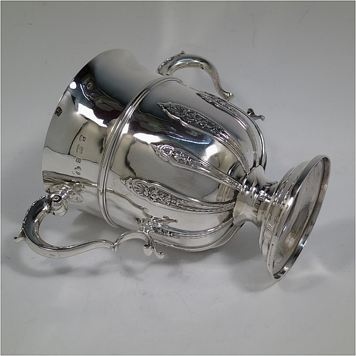 A very handsome Antique Edwardian Sterling Silver trophy cup, in a George II style, having a round body with applied floral strap-work decoration, two scroll side-handles with anthemion leaf thumb-pieces, a central applied girdle band, and all sitting on a stepped pedestal foot. Made by Elkington and Co., of Birmingham in 1908. The dimensions of this fine hand-made antique silver trophy cup are height 16 cms (6.3 inches), spread across arms 21 cms (8.25 inches), and it weighs approx. 510g (16.5 troy ounces).    