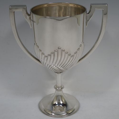 A handsome Antique Edwardian Sterling Silver trophy cup in a George III neoclassical style, having a round body with tapering sides and half-fluted decoration, two plain flat-topped side-handles, and all sitting on a pedestal foot with bead-edged borders. Made by Mappin and Webb of London in 1904. The dimensions of this fine hand-made antique silver trophy cup are height 23 cms (9 inches), spread across arms 18 cms (7 inches), and it weighs approx. 558g (18 troy ounces).    