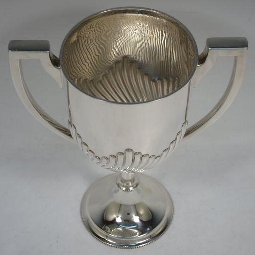 A handsome Antique Edwardian Sterling Silver trophy cup in a George III neoclassical style, having a round body with tapering sides and half-fluted decoration, two plain flat-topped side-handles, and all sitting on a pedestal foot with bead-edged borders. Made by Mappin and Webb of London in 1904. The dimensions of this fine hand-made antique silver trophy cup are height 23 cms (9 inches), spread across arms 18 cms (7 inches), and it weighs approx. 558g (18 troy ounces).    