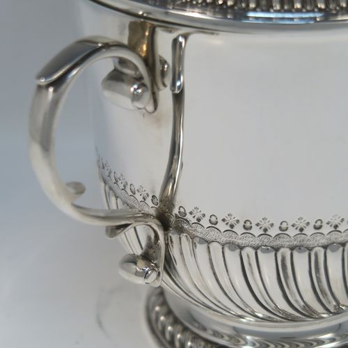 A very handsome Antique Edwardian Sterling Silver trophy cup and cover, in the shape of a lidded Porringer, having a round body with hand-chased half-fluted decoration, with two cast scroll side-handles, a lift-off cover with matching decoration and urn finial, and all sitting on a pedestal foot. This elegant silver cup and cover was made by Robert Comyns of London in 1910. The dimensions of this fine hand-made antique silver trophy porringer cup are height 21 cms (8.25 inches), spread across handles 24 cms (9.5 inches), and it weighs approx. 1,118g (36 troy ounces).   