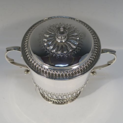 A very handsome Antique Edwardian Sterling Silver trophy cup and cover, in the shape of a lidded Porringer, having a round body with hand-chased half-fluted decoration, with two cast scroll side-handles, a lift-off cover with matching decoration and urn finial, and all sitting on a pedestal foot. This elegant silver cup and cover was made by Robert Comyns of London in 1910. The dimensions of this fine hand-made antique silver trophy porringer cup are height 21 cms (8.25 inches), spread across handles 24 cms (9.5 inches), and it weighs approx. 1,118g (36 troy ounces).   