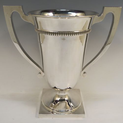 A large and handsome Art Deco style Sterling Silver trophy cup, having a plain round body with tapering sides, two plain square cross-section side-handles, with an applied upper band of geometric style decoration, and all sitting on a pedestal foot with a square base. This elegant Art Deco silver trophy cup was made by Mappin and Webb of London in 1927. The dimensions of this fine hand-made silver trophy cup and are height 32.5 cms (12.75 inches), spread across arms 31.5 cms (12.5 inches), and it weighs approx. 1,433g (46 troy ounces).   