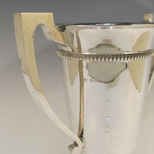 A large and handsome Art Deco style Sterling Silver trophy cup, having a plain round body with tapering sides, two plain square cross-section side-handles, with an applied upper band of geometric style decoration, and all sitting on a pedestal foot with a square base. This elegant Art Deco silver trophy cup was made by Mappin and Webb of London in 1927. The dimensions of this fine hand-made silver trophy cup and are height 32.5 cms (12.75 inches), spread across arms 31.5 cms (12.5 inches), and it weighs approx. 1,433g (46 troy ounces).   