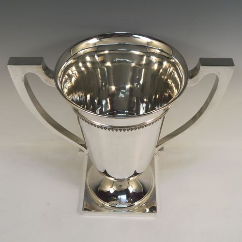 A large and handsome Art Deco style Sterling Silver trophy cup, having a plain round body with tapering sides, two plain square cross-section side-handles, with an applied upper band of geometric style decoration, and all sitting on a pedestal foot with a square base. This elegant Art Deco silver trophy cup was made by Mappin and Webb of London in 1927. The dimensions of this fine hand-made silver trophy cup and are height 32.5 cms (12.75 inches), spread across arms 31.5 cms (12.5 inches), and it weighs approx. 1,433g (46 troy ounces).   