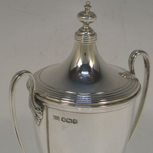 A very handsome Sterling Silver trophy cup and cover in a George III neoclassical style, having a round plain body with tapering sides, with hand-chased reeded borders, two looped side-handles, an original cover with matching decoration and cast knop finial, and all sitting on a pedestal foot. This beautiful silver trophy cup was made by Walker and Hall of Sheffield in 1927. The dimensions of this fine hand-made silver trophy cup and cover are height 18 cms (7 inches), spread across arms 11 cms (4.25 inches), and it weighs approx. 223g (7.2 troy ounces).   