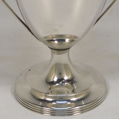 A very handsome Sterling Silver trophy cup and cover in a George III neoclassical style, having a round plain body with tapering sides, with hand-chased reeded borders, two looped side-handles, an original cover with matching decoration and cast knop finial, and all sitting on a pedestal foot. This beautiful silver trophy cup was made by Walker and Hall of Sheffield in 1927. The dimensions of this fine hand-made silver trophy cup and cover are height 18 cms (7 inches), spread across arms 11 cms (4.25 inches), and it weighs approx. 223g (7.2 troy ounces).   