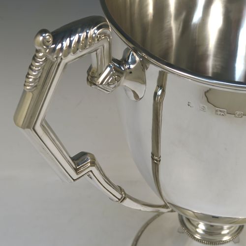 A large and very handsome Sterling Silver trophy cup, having a plain round body with tapering sides, two reeded side-handles with anthemion leaf thumb-pieces, and all sitting on a plain round pedestal foot with applied bead-edged borders. This elegant trophy cup was hallmarked for Birmingham in 1931. The dimensions of this fine hand-made silver trophy cup are height 43 cms (17 inches), spread across arms 39 cms (15.3 inches), and it weighs approx. 1,727g (55.7 troy ounces).  