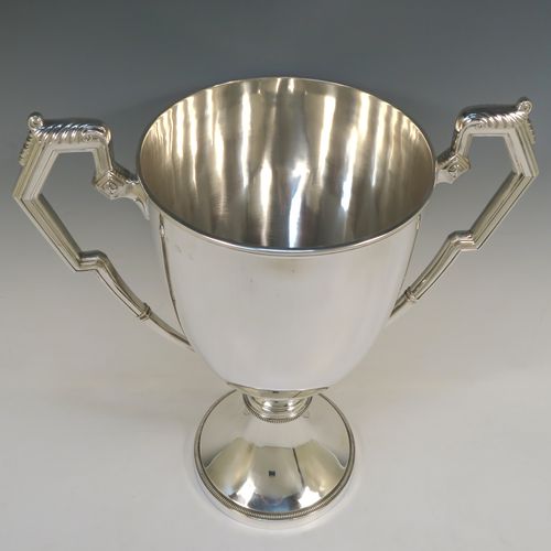 A large and very handsome Sterling Silver trophy cup, having a plain round body with tapering sides, two reeded side-handles with anthemion leaf thumb-pieces, and all sitting on a plain round pedestal foot with applied bead-edged borders. This elegant trophy cup was hallmarked for Birmingham in 1931. The dimensions of this fine hand-made silver trophy cup are height 43 cms (17 inches), spread across arms 39 cms (15.3 inches), and it weighs approx. 1,727g (55.7 troy ounces).  