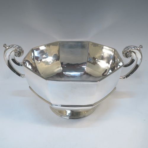 A very handsome and heavy Antique Edwardian Sterling Silver two-handled trophy bowl, having a plain hexagonal panelled body with an applied central reeded band, two cast scroll side-handles with anthemion leaf thumb-pieces, and sitting on a plain round pedestal foot. This elegant antique silver trophy bowl was made by Henry Lambert of London in 1903. The dimensions of this fine hand-made sterling silver trophy cup bowl are height 23 cms (9 inches), width across handles 46 cms (18 inches), and it weighs approx. 2,345g (75.6 troy ounces).  