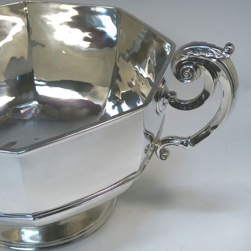 A very handsome and heavy Antique Edwardian Sterling Silver two-handled trophy bowl, having a plain hexagonal panelled body with an applied central reeded band, two cast scroll side-handles with anthemion leaf thumb-pieces, and sitting on a plain round pedestal foot. This elegant antique silver trophy bowl was made by Henry Lambert of London in 1903. The dimensions of this fine hand-made sterling silver trophy cup bowl are height 23 cms (9 inches), width across handles 46 cms (18 inches), and it weighs approx. 2,345g (75.6 troy ounces).  