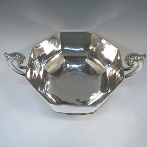 A very handsome and heavy Antique Edwardian Sterling Silver two-handled trophy bowl, having a plain hexagonal panelled body with an applied central reeded band, two cast scroll side-handles with anthemion leaf thumb-pieces, and sitting on a plain round pedestal foot. This elegant antique silver trophy bowl was made by Henry Lambert of London in 1903. The dimensions of this fine hand-made sterling silver trophy cup bowl are height 23 cms (9 inches), width across handles 46 cms (18 inches), and it weighs approx. 2,345g (75.6 troy ounces).  