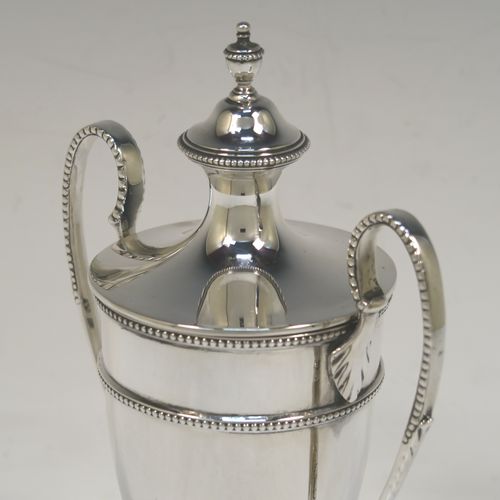 A small but very elegant Antique Sterling Silver trophy cup and cover in a George III neoclassical style, having a round plain body with tapering sides, with applied bead-edged borders, two looped side-handles, an original cover with matching decoration and cast urn finial, and all sitting on a pedestal foot. This handsome silver trophy cup was made by William Hutton of Sheffield in 1912. The dimensions of this fine hand-made silver trophy cup and cover are height 20 cms (8 inches), spread across arms 12.5 cms (5 inches), and it weighs approx. 280g (9 troy ounces).   