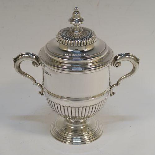 A fantastic quality Sterling Silver trophy cup and cover, having a round body with hand-chased half-fluted, with two cast scroll side-handles, a lift-off cover with matching decoration and a cast urn-shaped finial, and all sitting on a stepped pedestal foot. This very handsome silver trophy cup and cover was made by Henry Phillips of London in 193.5 The dimensions of this fine hand-made silver trophy cup are height 15 cms (6 inches), spread across handles 14.5 cms (5.75 inches), and it weighs approx. 375g (12 troy ounces).  