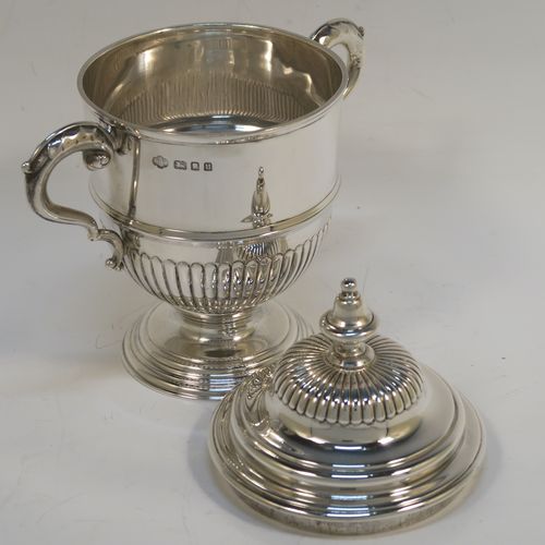 A fantastic quality Sterling Silver trophy cup and cover, having a round body with hand-chased half-fluted, with two cast scroll side-handles, a lift-off cover with matching decoration and a cast urn-shaped finial, and all sitting on a stepped pedestal foot. This very handsome silver trophy cup and cover was made by Henry Phillips of London in 193.5 The dimensions of this fine hand-made silver trophy cup are height 15 cms (6 inches), spread across handles 14.5 cms (5.75 inches), and it weighs approx. 375g (12 troy ounces).  