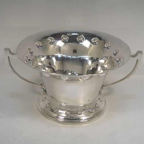 A very unusual Arts and Crafts style Antique Edwardian Sterling Silver two-handled trophy bowl, having a plain round body with flaring sides and an upper band of hand-chased balls, with two plain cast side-handles, and all sitting on a round pedestal foot with matching decoration. This beautiful antique silver Arts and Crafts trophy bowl was made by Wakely and Wheeler of London in 1910. The dimensions of this fine hand-made antique sterling silver trophy cup bowl are height 13 cms (5 inches), width across handles 27 cms (10.75 inches), and it weighs approx. 797g (25.7 troy ounces).   