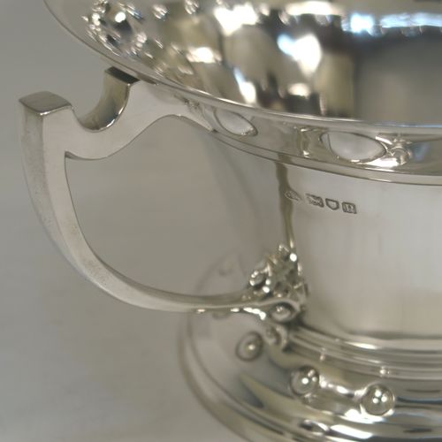 A very unusual Arts and Crafts style Antique Edwardian Sterling Silver two-handled trophy bowl, having a plain round body with flaring sides and an upper band of hand-chased balls, with two plain cast side-handles, and all sitting on a round pedestal foot with matching decoration. This beautiful antique silver Arts and Crafts trophy bowl was made by Wakely and Wheeler of London in 1910. The dimensions of this fine hand-made antique sterling silver trophy cup bowl are height 13 cms (5 inches), width across handles 27 cms (10.75 inches), and it weighs approx. 797g (25.7 troy ounces).   