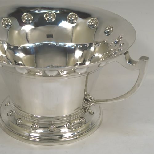 A very unusual Arts and Crafts style Antique Edwardian Sterling Silver two-handled trophy bowl, having a plain round body with flaring sides and an upper band of hand-chased balls, with two plain cast side-handles, and all sitting on a round pedestal foot with matching decoration. This beautiful antique silver Arts and Crafts trophy bowl was made by Wakely and Wheeler of London in 1910. The dimensions of this fine hand-made antique sterling silver trophy cup bowl are height 13 cms (5 inches), width across handles 27 cms (10.75 inches), and it weighs approx. 797g (25.7 troy ounces).   