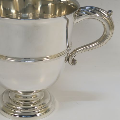 A very handsome Sterling Silver trophy cup in a George III neoclassical style, having a round plain body with tapering sides, an applied central reeded band, two cast scroll side-handles, and all sitting on a stepped pedestal foot. This elegant silver trophy cup was made by Fordham and Faulkner of Sheffield in 1925. The dimensions of this fine hand-made silver trophy cup are height 18 cms (7 inches), spread across arms 27 cms (10.5 inches), and it weighs approx. 620g (20 troy ounces).   