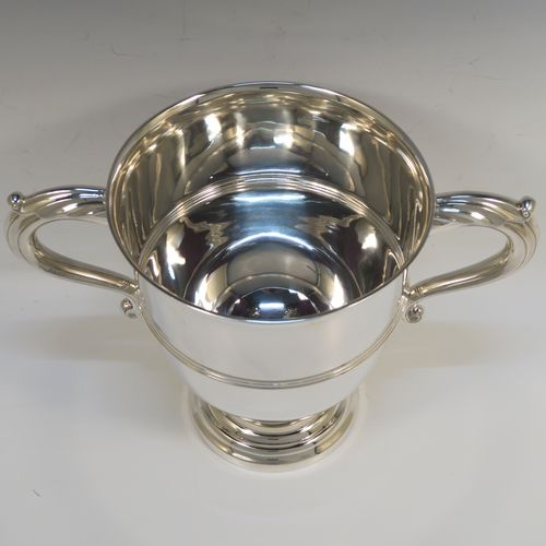 A very handsome Sterling Silver trophy cup in a George III neoclassical style, having a round plain body with tapering sides, an applied central reeded band, two cast scroll side-handles, and all sitting on a stepped pedestal foot. This elegant silver trophy cup was made by Fordham and Faulkner of Sheffield in 1925. The dimensions of this fine hand-made silver trophy cup are height 18 cms (7 inches), spread across arms 27 cms (10.5 inches), and it weighs approx. 620g (20 troy ounces).   