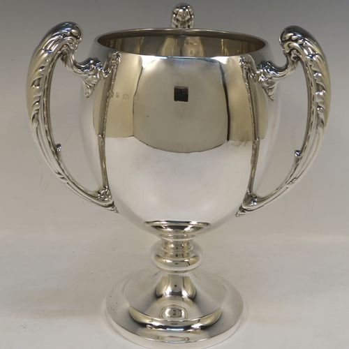 A handsome Sterling Silver trophy loving cup, having a plain round bellied body, three cast scroll side-handles with anthemion leaf decoration, and sitting on a plain round pedestal foot. This elegant silver three-handled loving cup trophy was made by Elkington & Co., of Birmingham in 1932. The dimensions of this fine hand-made silver trophy loving cup are height 26 cms (10.25 inches), width across handles 21.5 cms (8.5 inches), and it weighs approx. 852g (27.5 troy ounces).   