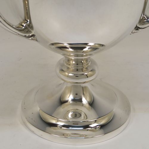 A handsome Sterling Silver trophy loving cup, having a plain round bellied body, three cast scroll side-handles with anthemion leaf decoration, and sitting on a plain round pedestal foot. This elegant silver three-handled loving cup trophy was made by Elkington & Co., of Birmingham in 1932. The dimensions of this fine hand-made silver trophy loving cup are height 26 cms (10.25 inches), width across handles 21.5 cms (8.5 inches), and it weighs approx. 852g (27.5 troy ounces).   