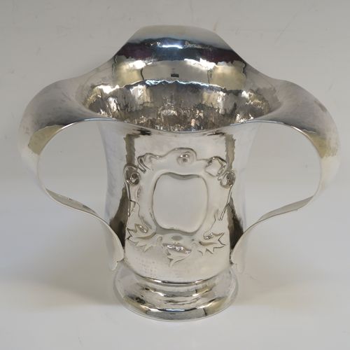 A very unusual Sterling Silver Art and Crafts style trophy loving cup, having a round body with hand-hammered decoration, three scroll side handles, a hand-chased floral and scroll vacant cartouche on one side, and all sitting on a pedestal foot. This beautiful Arts and Crafts style loving cup was made by Francis Higgins and Son Ltd., of London in 1925. The dimensions of this fine hand-made silver three-handled trophy loving cup are height 13 cms (5 inches), width across handles 16 cms (6.25 inches), and it weighs approx. 381g (12.3 troy ounces).   