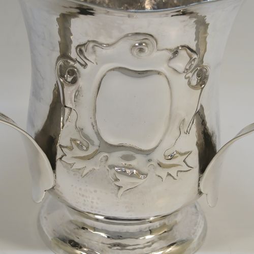 A very unusual Sterling Silver Art and Crafts style trophy loving cup, having a round body with hand-hammered decoration, three scroll side handles, a hand-chased floral and scroll vacant cartouche on one side, and all sitting on a pedestal foot. This beautiful Arts and Crafts style loving cup was made by Francis Higgins and Son Ltd., of London in 1925. The dimensions of this fine hand-made silver three-handled trophy loving cup are height 13 cms (5 inches), width across handles 16 cms (6.25 inches), and it weighs approx. 381g (12.3 troy ounces).   