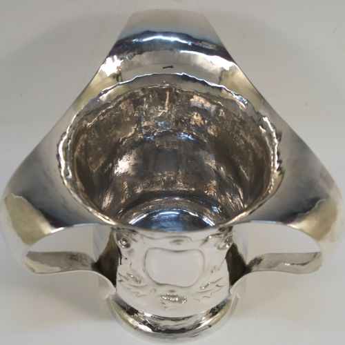 A very unusual Sterling Silver Art and Crafts style trophy loving cup, having a round body with hand-hammered decoration, three scroll side handles, a hand-chased floral and scroll vacant cartouche on one side, and all sitting on a pedestal foot. This beautiful Arts and Crafts style loving cup was made by Francis Higgins and Son Ltd., of London in 1925. The dimensions of this fine hand-made silver three-handled trophy loving cup are height 13 cms (5 inches), width across handles 16 cms (6.25 inches), and it weighs approx. 381g (12.3 troy ounces).   