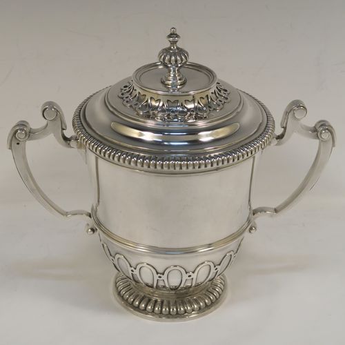 A fantastic quality Antique style Sterling Silver trophy cup and cover, having a mainly plain round body with applied melon fluting and gadroon borders, with two cast scroll side-handles, a lift-off cover with matching decoration and a cast urn-shaped finial, and all sitting on a pedestal foot. This very handsome antique silver trophy cup and cover was made by Mappin and Webb of London in 1931. The dimensions of this fine hand-made antique silver trophy cup are height 18.5 cms (7.25 inches), spread across handles 21 cms (8.25 inches), and it weighs approx. 788g (25 troy ounces).   