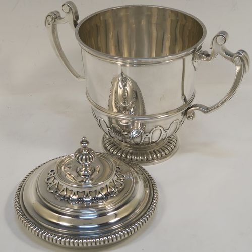 A fantastic quality Antique style Sterling Silver trophy cup and cover, having a mainly plain round body with applied melon fluting and gadroon borders, with two cast scroll side-handles, a lift-off cover with matching decoration and a cast urn-shaped finial, and all sitting on a pedestal foot. This very handsome antique silver trophy cup and cover was made by Mappin and Webb of London in 1931. The dimensions of this fine hand-made antique silver trophy cup are height 18.5 cms (7.25 inches), spread across handles 21 cms (8.25 inches), and it weighs approx. 788g (25 troy ounces).   