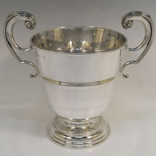 A very handsome Antique Sterling Silver trophy cup in a George II style, having a plain round body with applied reeded borders, two flying scroll side-handles, a central applied girdle band, and all sitting on a stepped pedestal foot. This elegant antique silver trophy cup was made in Birmingham in 1911. The dimensions of this fine hand-made antique silver trophy cup are height 23 cms (9 inches), spread across arms 26 cms (10.25 inches), and it weighs approx. 861g (27.8 troy ounces).   