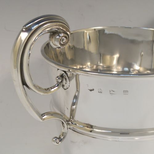 A very handsome Antique Sterling Silver trophy cup in a George II style, having a plain round body with applied reeded borders, two flying scroll side-handles, a central applied girdle band, and all sitting on a stepped pedestal foot. This elegant antique silver trophy cup was made in Birmingham in 1911. The dimensions of this fine hand-made antique silver trophy cup are height 23 cms (9 inches), spread across arms 26 cms (10.25 inches), and it weighs approx. 861g (27.8 troy ounces).   