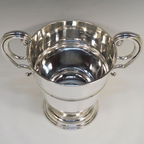 A very handsome Antique Sterling Silver trophy cup in a George II style, having a plain round body with applied reeded borders, two flying scroll side-handles, a central applied girdle band, and all sitting on a stepped pedestal foot. This elegant antique silver trophy cup was made in Birmingham in 1911. The dimensions of this fine hand-made antique silver trophy cup are height 23 cms (9 inches), spread across arms 26 cms (10.25 inches), and it weighs approx. 861g (27.8 troy ounces).   