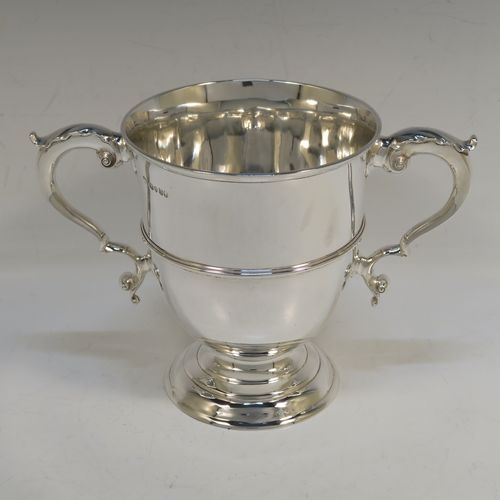 A very elegant and classical Antique Victorian Sterling Silver trophy loving cup, having a plain round body with a central reeded band, two anthemion leaf topped scroll side-handles, and sitting on a round pedestal foot. This handsome antique silver loving cup trophy was made by D. and C. Houle of London in 1875. The dimensions of this fine antique silver loving cup are height 14.5 cms (5.75 inches), spread across handles 21.5 cms (8.5 inches), and it weighs approx. 470g (15 troy ounces).   