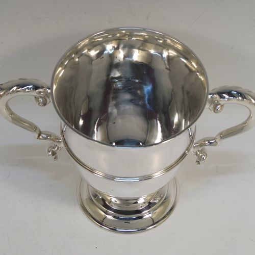 A very elegant and classical Antique Victorian Sterling Silver trophy loving cup, having a plain round body with a central reeded band, two anthemion leaf topped scroll side-handles, and sitting on a round pedestal foot. This handsome antique silver loving cup trophy was made by D. and C. Houle of London in 1875. The dimensions of this fine antique silver loving cup are height 14.5 cms (5.75 inches), spread across handles 21.5 cms (8.5 inches), and it weighs approx. 470g (15 troy ounces).   