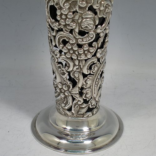 An Antique Victorian Sterling Silver pair of vases, having hand-chased and pierced bodies with floral decoration on round tapering sides, with vacant cartouches on one side, removable blue-glass liners, with wavy-edge rims and and sitting on pedestal feet. Made by the William Comyns of London in 1897. The dimensions of this fine hand-made pair of antique silver vases are height 18 cms (7 inches), diameter at top 9 cms (3.5 inches), and they weigh a total of 272g (8.8 troy ounces).   