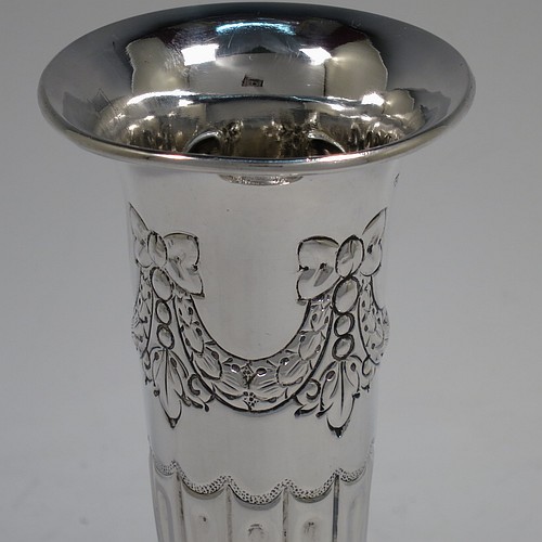 A very pretty Antique Victorian Sterling Silver pair of table flower vases, having round bodies with tapering sides and hand-chased neoclassical style decoration with half-fluting, ribbon bows, and swags, and sitting on pedestal feet. Made by Henry Atkins of Sheffield in 1892. The dimensions of these fine hand-made antique silver pair of vases are height 15 cms (6 inches), diameter at top 6.5 cms (2.5 inches), and they weigh at total of approx. 200g (6.5 troy ounces). Please note that these vases are not loaded.    