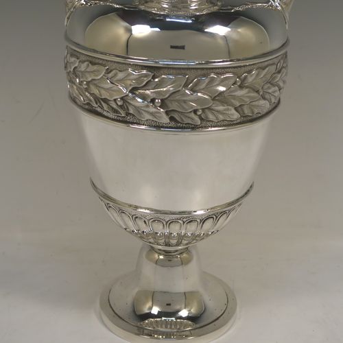 A large and heavy Antique Victorian Sterling Silver Neoclassical style single vase, having an amphora shape with a round body and hand-chased bands of floral, anthemion leaf, and fluted decoration, with two cast side handles, and all sitting on a plain round pedestal foot. This beautiful large antique silver vase was made by William Hutton and Sons of London in 1893. The dimensions of this fine hand-made antique silver vase are height 39 cms (15.3 inches), spread across arms 19 cms (7.5 inches), diameter of body at widest point 15 cms (6 inches), and it weighs approx. 1,117g (36 troy ounces). Please note that this vase is not loaded.   