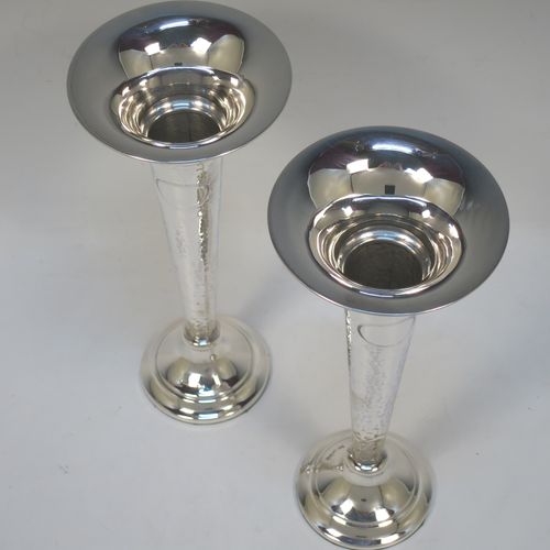 A handsome and stylish Antique Sterling Silver pair of table flower vases, having plain round tops, tapering bodies with hand-hammered decoration and oval vacant cartouches, and sitting on round stepped pedestal bases. Made by Walker and Hall of Sheffield in 1919. The dimensions of these fine hand-made pair of antique silver vases are height 22 cms (8.5 inches), and diameter at top 9 cms (3.5 inches).   