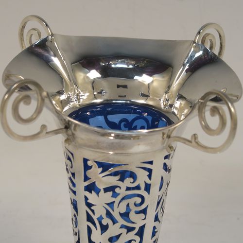 A vert pretty pair of Antique Edwardian Sterling Silver vases, having hand-pierced bodies with floral decoration on round tapering sides, with removable blue-glass liners, with wavy-edge rims and four scroll handles, and all sitting on plain round pedestal feet. These beautiful antique silver vases were made by Harrison and Hipwood of Birmingham in 1910. The dimensions of this fine hand-made pair of antique silver vases are height 13 cms (5.25 inches), and diameter at top 10 cms (4 inches).   