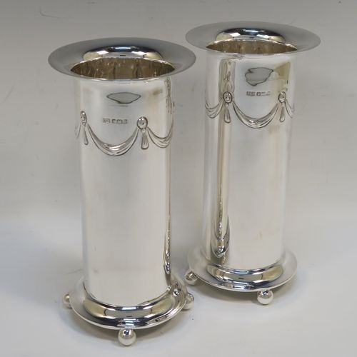 A very handsome pair of Antique Edwardian Sterling Silver table flower vases, having round straight-sided bodies with a top band of hand-chased neoclassical bow and swag style decoration, and sitting on four ball feet. These elegant silver vases were made by Roberts and Belk of Sheffield in 1907. The dimensions of these fine hand-made antique silver pair of vases are height 18.5 cms (7.25 inches), diameter at top 9 cms (3.5 inches), and they weigh at total of approx. 434g (14 troy ounces). Please note that these vases are not loaded.   