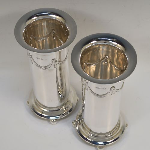 A very handsome pair of Antique Edwardian Sterling Silver table flower vases, having round straight-sided bodies with a top band of hand-chased neoclassical bow and swag style decoration, and sitting on four ball feet. These elegant silver vases were made by Roberts and Belk of Sheffield in 1907. The dimensions of these fine hand-made antique silver pair of vases are height 18.5 cms (7.25 inches), diameter at top 9 cms (3.5 inches), and they weigh at total of approx. 434g (14 troy ounces). Please note that these vases are not loaded.   