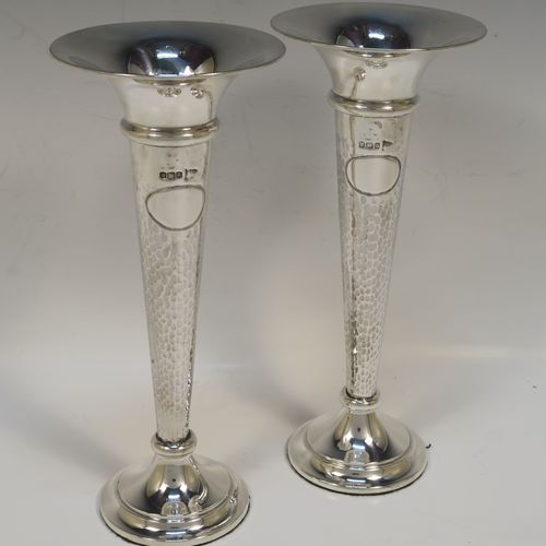 A handsome and stylish Antique Edwardian Sterling Silver pair of table flower vases, having plain round tops, tapering bodies with hand-hammered decoration and oval vacant cartouches, and sitting on round stepped pedestal bases. These elegant silver vases were made by Walker and Hall of Sheffield in 1909. The dimensions of these fine hand-made pair of antique silver vases are height 22 cms (8.5 inches), and diameter at top 9 cms (3.5 inches).   