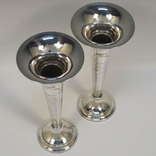 A handsome and stylish Antique Edwardian Sterling Silver pair of table flower vases, having plain round tops, tapering bodies with hand-hammered decoration and oval vacant cartouches, and sitting on round stepped pedestal bases. These elegant silver vases were made by Walker and Hall of Sheffield in 1909. The dimensions of these fine hand-made pair of antique silver vases are height 22 cms (8.5 inches), and diameter at top 9 cms (3.5 inches).   